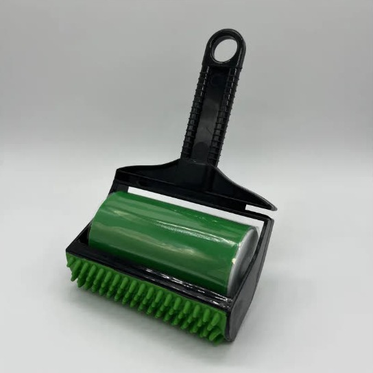 Large black pet hair roller with a green sticky roller and a green rubber-bristled edge, held by a black handle with a hanging loop, on a plain grey background
